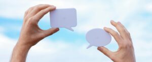 Close-up of hands holding speech bubbles, symbolizing communication and dialogue against a blue sky.